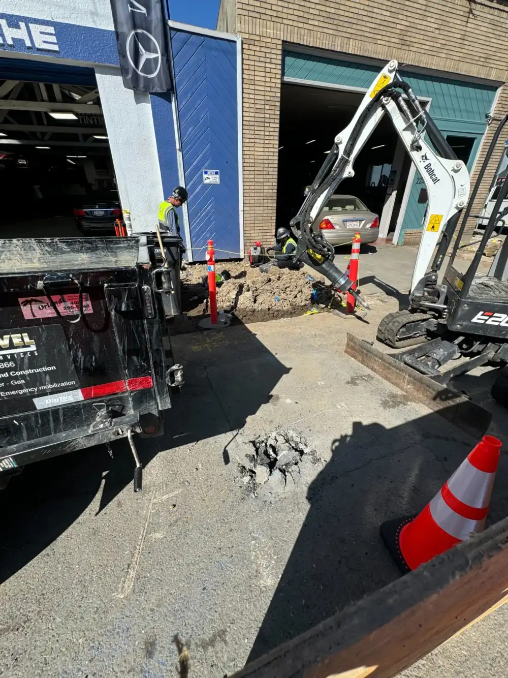 Mini excavator with a breaker attachment opening a utility trench in hard Bay Area soil