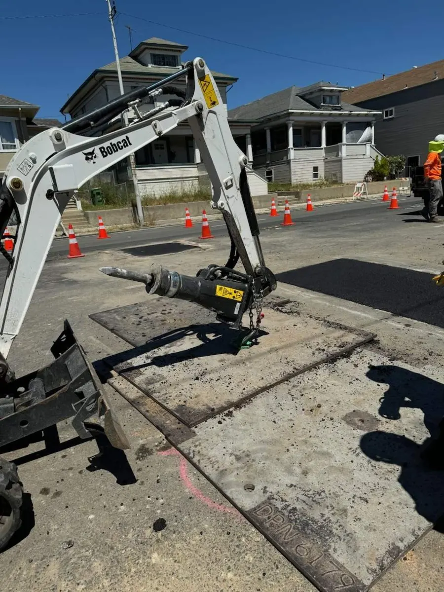 Excavator working beside steel trench plates laid across the street
